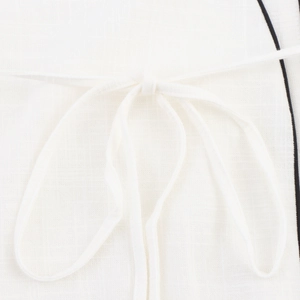 Detail shot of white cotton-linen fabric with contrast piping and knotted tie closure