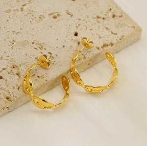Detail of gold titanium C-shaped hoop earrings with coffee bean link texture on travertine
