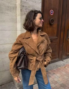 Detail of a brown faux suede jacket with lapel and waist belt in a street setting
