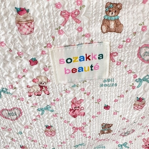 Close-up of white quilted fabric with cute teddy bears, strawberries and floral embroidery