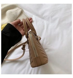 Detailed close-up of khaki quilted handbag with V-shaped stitching and golden zipper