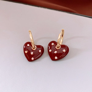 Close-up of heart-shaped gold earrings with dark red glaze and sparkling rhinestones