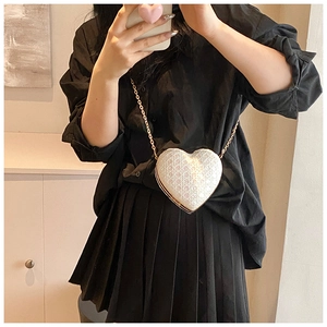 Detailed view of white heart-shaped crossbody bag with gold chain strap on female model
