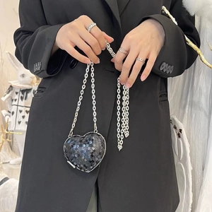 Close-up of heart-shaped black sequin mini bag with silver metal chain on model