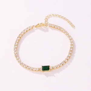 Detailed view of gold tennis bracelet featuring CZ stones and green center emerald