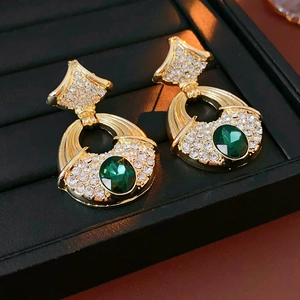 Detail showing vintage gold earrings with emerald green oval stone and sparkling rhinestones