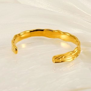 Detail view of irregular wavy gold-plated titanium steel open bangle on stone surface