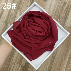 Détail macro du hijab en mousseline rouge vin avec paillettes argentées sur un plateau