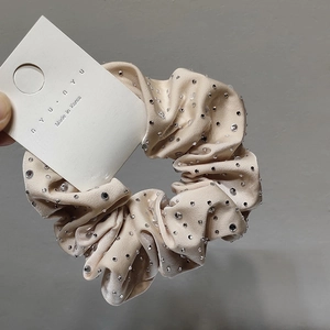 Close-up of beige satin scrunchie with rhinestones on an authentic branding card
