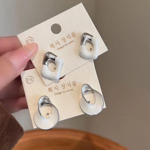 Close-up of geometric white enamel stud earrings with silver-plated twisted design