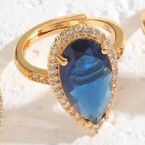 Macro view of gold ring with pear-shaped blue gemstone and micro-paved zirconia halo
