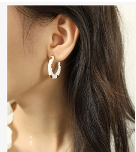 Close-up of model wearing C-shaped enamel earrings in white and gold splatter pattern