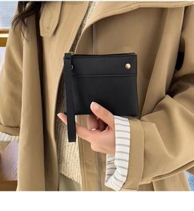 Black leather coin purse with gold zipper and wrist strap held by a person