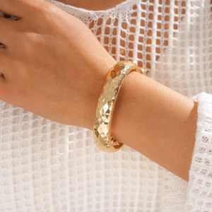 Detail eines goldenen breiten Armreifs mit diamantgeschliffener Textur an einem Model
