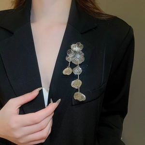Detailed close-up of a silver floral brooch with mesh petals and tassels on a black suit