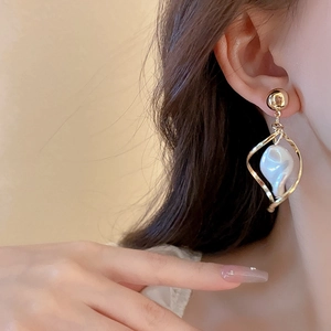 Detailed view of a gold star-shaped twisted earring with an irregular white pearl on model