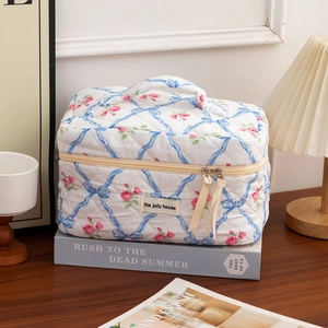 Macro shot of quilted makeup bag with pink roses and blue ribbons on a wooden desk