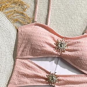 Detail of pink bubble texture swimsuit with golden sun-shaped metal hardware and cut-out