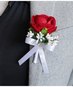 Close-up of a red velvet rose boutonniere with green leaves and a sparkling rhinestone bow