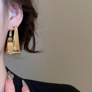 Close-up of golden geometric trapezoid hoop earrings worn by a model for a modern look