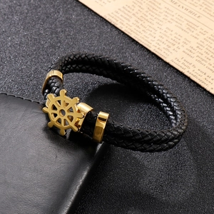Detail of black braided leather bracelet featuring a golden stainless steel rudder clasp