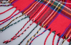 Close-up of red plaid hooded poncho with detailed woven fringe tassels and soft acrylic texture