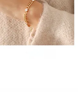 Detailed shot of a gold textured necklace with round zircons on a beige sweater sleeve