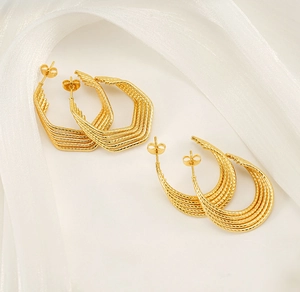 Detail of geometric hexagon and C-shape earrings with layered gold textures on white silk