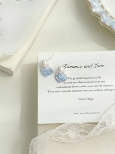 Macro detail of silver shell earrings with blue crystal and white pearl in a romantic setting