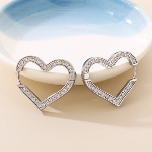 Close-up of heart-shaped steel earrings with micro-inlaid cubic zirconia on a ceramic tray