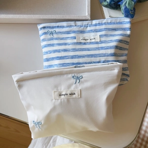 Close-up of blue bow embroidery and simple wish label on striped canvas makeup bags