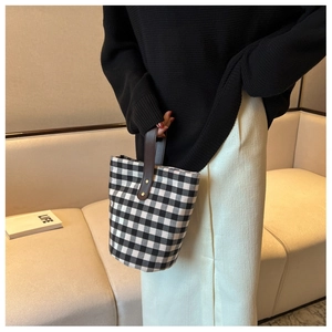 Close-up of checkerboard canvas bucket bag with brown leather handle in a lifestyle setting