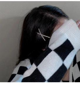 Close-up of golden X-shaped hair clip with sparkling rhinestones on black hair
