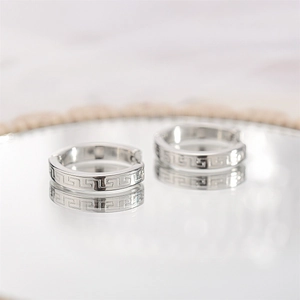 Macro shot of silver stainless steel hoop earrings featuring intricate Greek fret pattern