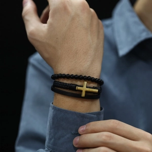 Close-up of black braided leather bracelet with golden cross charm on male wrist