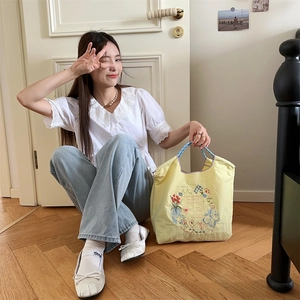 Détail de broderie florale sur tote bag en tissu Oxford jaune avec anses bleues