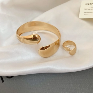 Detailed view of polished gold minimalist open bracelet and matching ring on silk fabric