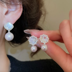 Close-up of pearl drop earrings featuring intricate flower zircon studs on silver posts