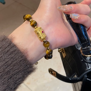 Detail of tiger eye stone bracelet with golden embossed bead on a woman wrist