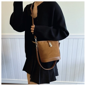 Brown leather bucket bag with adjustable shoulder strap worn by a model against a white wall