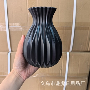 Detail of a black geometric textured flower vase with diamond facets held by hand