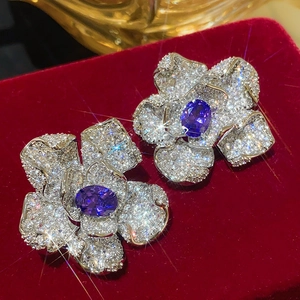 Macro shot of silver flower earrings with pavé crystals and deep blue gemstone center