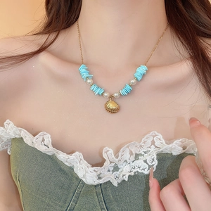 Close-up of starfish shell and pearl pendant necklace with blue stones on a model