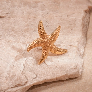 Detailed close-up of a golden metal starfish ring on a natural warm textured stone