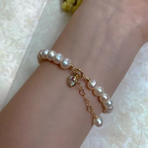 Baroque pearl bracelet detail with 14K gold-plated heart chain and gemstone charm