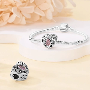 Macro shot of a silver heart-shaped charm with pink crystal inlay and hollow floral patterns
