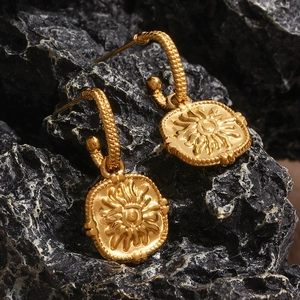 Macro view of gold stainless steel sun totem hoop earrings on a black stone background