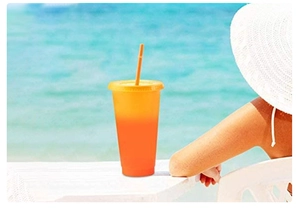 Detail van oranje kleurveranderende beker met rietje in een zonnige strandomgeving