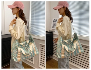 On-shoulder view of large canvas travel bag with blue and beige letter prints