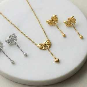 Minimalist gold and silver bow heart pendant necklace and earring jewelry set on marble
